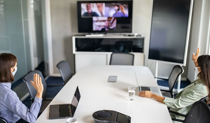 Two masked women in a conference room conducting a hybrid virtual/in person meeting